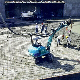 Pump truck with excavator assistance pouring new concrete slab